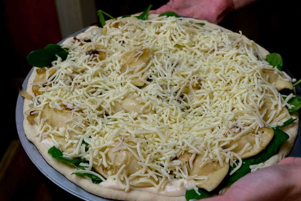 Top cheesy pierogi pizza with plenty of shredded Mozzarella cheese!